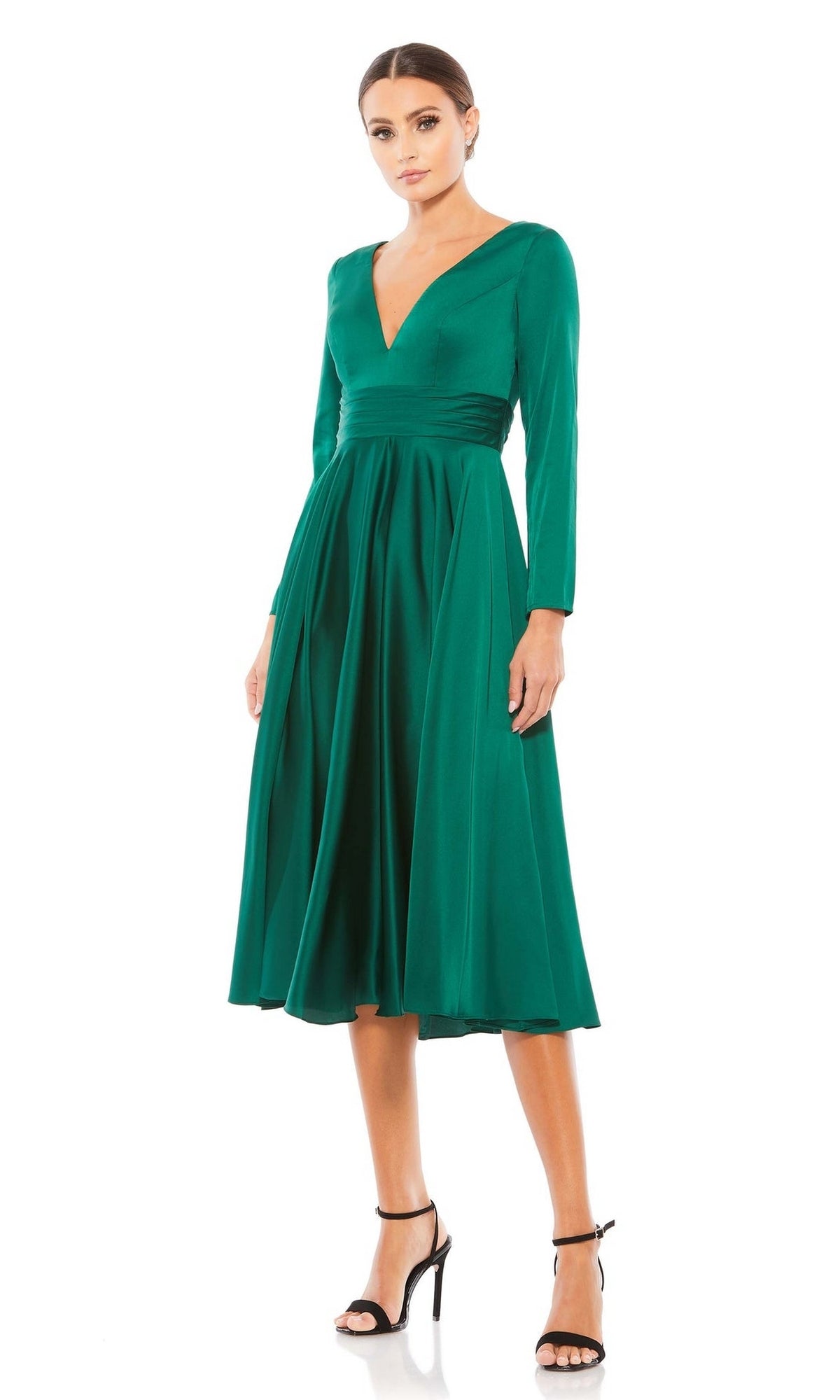 A woman models the Mac Duggal 67527 Emerald Midi Wedding Guest Dress with long sleeves and a V-neck, paired with black high-heeled sandals, standing against a plain white backdrop.